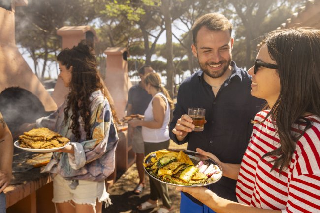 Persone che cucinano e sorridono all'aperto.