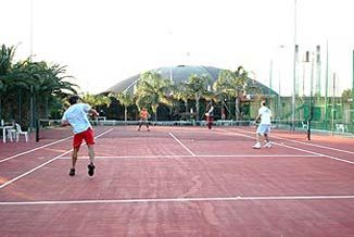 Persone che giocano a tennis su un campo all'aperto con palme sullo sfondo.