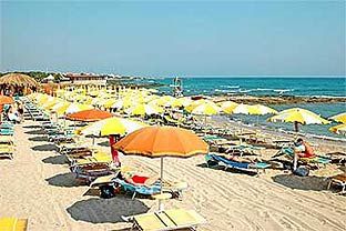 Spiaggia con lettini e ombrelloni gialli e arancioni su sabbia chiara.
