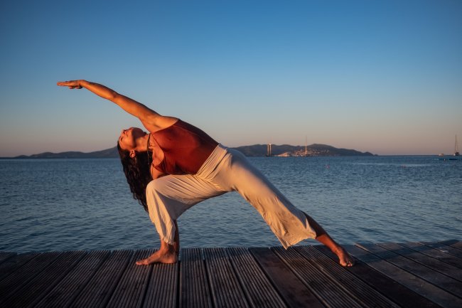 Donna fa yoga al tramonto su un molo.