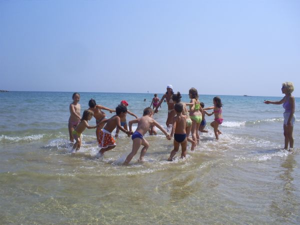 Bambini giocano in mare, formando un cerchio con gli adulti che li osservano.