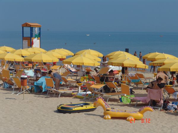 Spiaggia affollata con lettini e ombrelloni gialli vicino al mare.