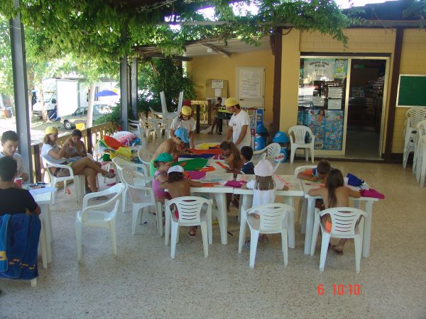 Bambini seduti a tavoli sotto un pergolato, impegnati in attività creative.