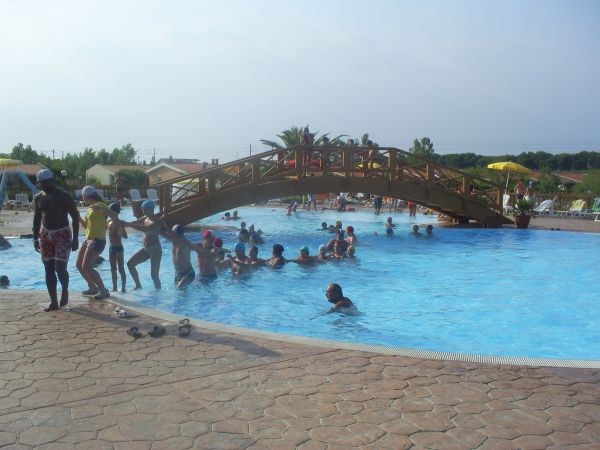 Persone nuotano e chiacchierano vicino a un ponte di legno sopra una piscina.