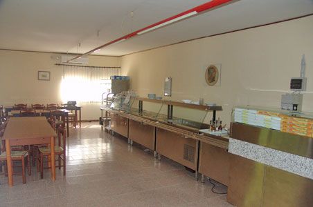 Sala da pranzo semplice con tavoli, sedie e banco self-service.