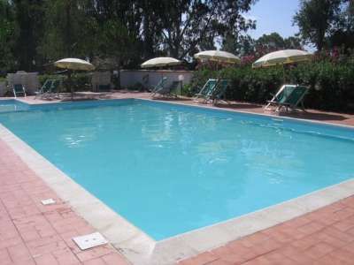 Una piscina all'aperto circondata da sedie a sdraio e ombrelloni, immersa nel verde.