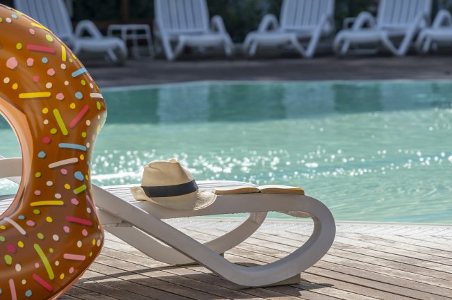 Ciambella gonfiabile e cappello su sedia a sdraio vicino a piscina.