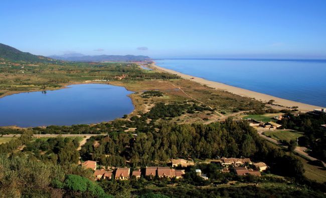 Paesaggio costiero con lago, spiaggia e vegetazione lussureggiante.