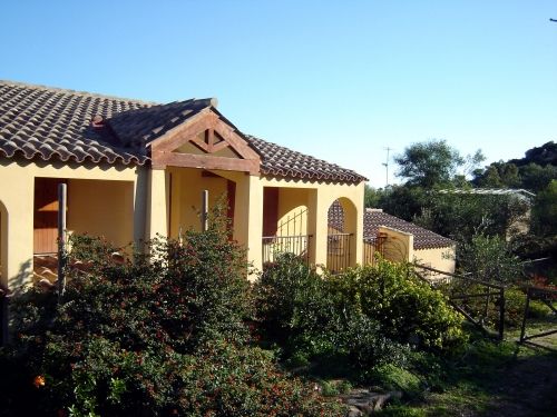 Casa con tetto in tegole, circondata da arbusti verdi.