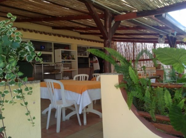 Terrazza coperta con piante, sedie bianche e tavoli con tovaglie arancioni.