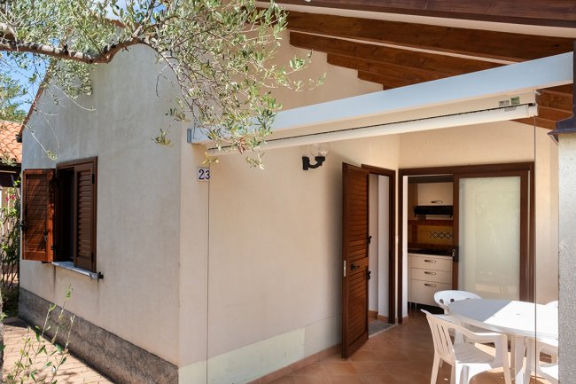 Esterno di una piccola casa con portico e tavolo bianco.