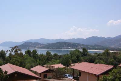 Tetti di case tra alberi con vista su una baia e colline in lontananza.