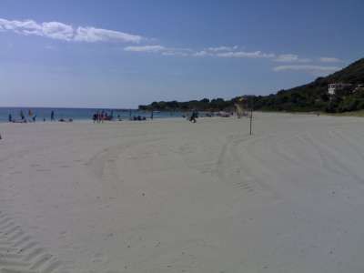 Spiaggia sabbiosa con mare in lontananza e alcune persone.