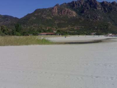 Spiaggia sabbiosa con montagne sullo sfondo e vegetazione verde, cielo sereno.