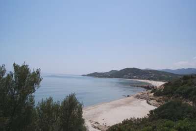 Una spiaggia sabbiosa con acqua calma, contornata da vegetazione e colline in lontananza.