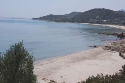 Spiaggia con sabbia chiara e mare tranquillo, colline verdi sullo sfondo.