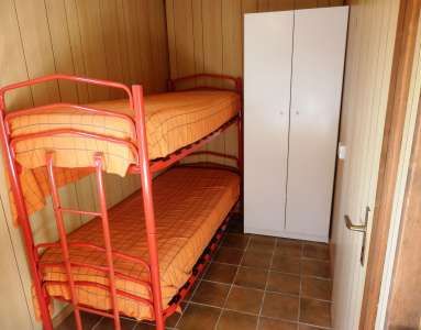 Letto a castello con struttura rossa e materassi arancioni in una stanza con armadio bianco.