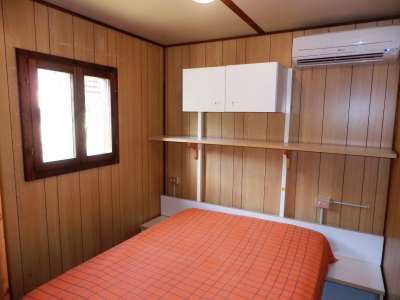 Letto matrimoniale arancione in una camera con pareti di legno, finestra e condizionatore.