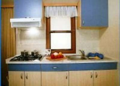 Cucina con mobili blu, lavello, fornelli e finestrella sopra il piano di lavoro.