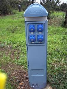 Colonnina blu con prese elettriche all'aperto, situata su erba.