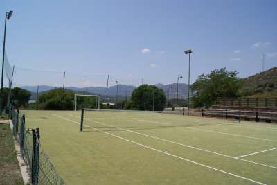 Campo da tennis all'aperto, con rete e recinzione, circondato da colline.