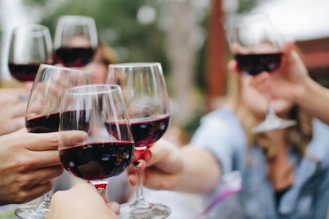Persone brindano con bicchieri di vino rosso.