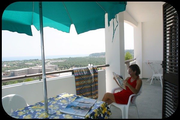 Donna seduta su un balcone con vista mare.