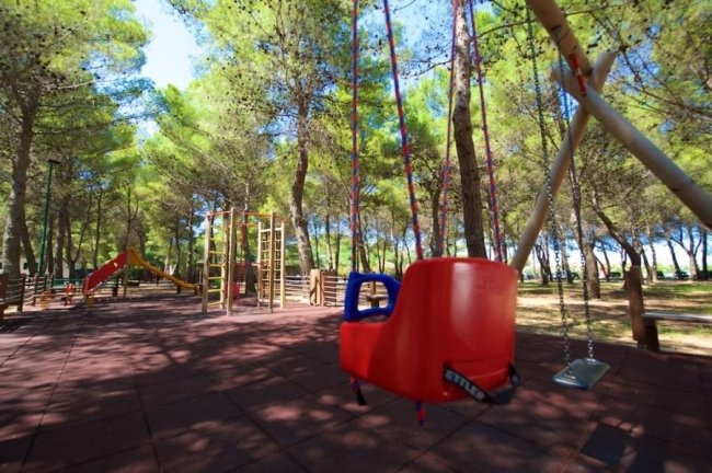 Altalena e giochi per bambini in un parco alberato.