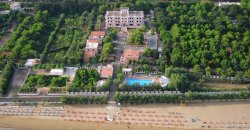 Vista aerea di un complesso con piscina, immerso nel verde, vicino a una spiaggia.