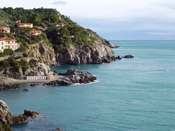 Scogliera con case e mare azzurro, piccola spiaggia rocciosa.