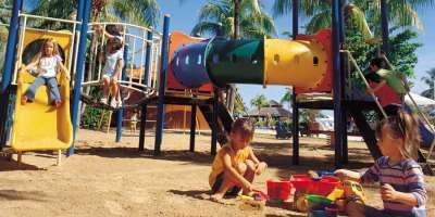 Bambini giocano in un parco giochi colorato con scivoli e tunnel.