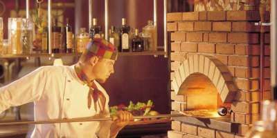 Cuoco che inforna una pizza in un forno a legna.