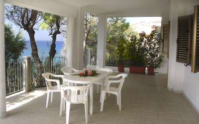 Tavolo e sedie bianche su una veranda con vista sul mare.