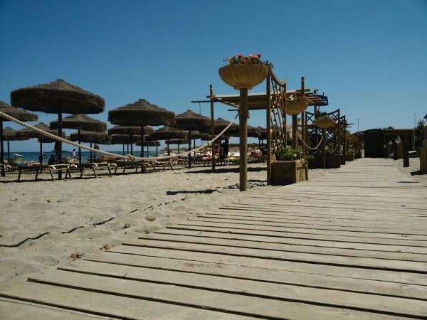 Passeggiata in legno sulla spiaggia con ombrelloni di paglia.