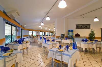 Una sala da pranzo con tavoli apparecchiati con tovaglie bianche e decorazioni blu.