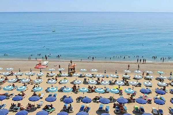 Spiaggia affollata con ombrelloni e lettini blu.