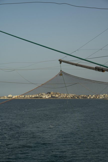 Reti da pesca sopra il mare con città sullo sfondo.