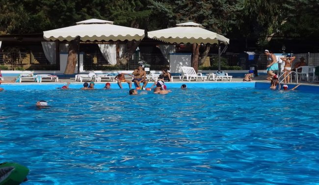 Piscina con ombrelloni bianchi, persone nuotano.