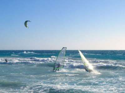 Persone che praticano windsurf e kitesurf su onde blu.