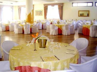 Sala da pranzo con tavoli rotondi apparecchiati e sedie coperte di bianco.