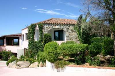 Casa in pietra con tetto a spiovente e giardino rigoglioso, cielo limpido.