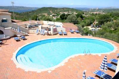 Piscina a forma di fagiolo circondata da lettini e ombrelloni. Vista panoramica.