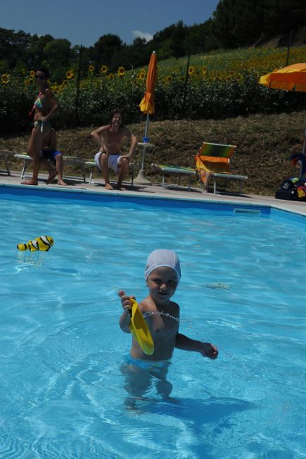 Bambino in piscina con cuffia e giocattolo giallo.
