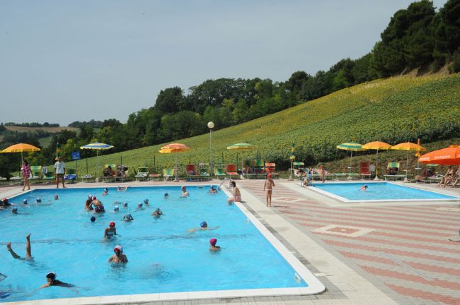 Due piscine con persone, colline e ombrelloni.