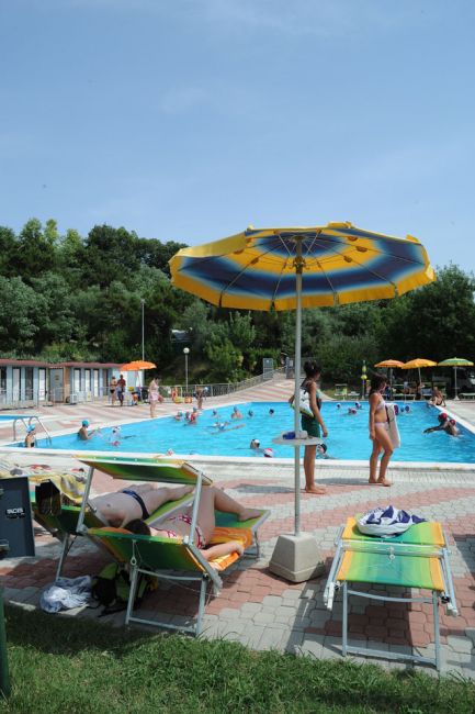 Piscina all'aperto con ombrelloni colorati e persone in relax.