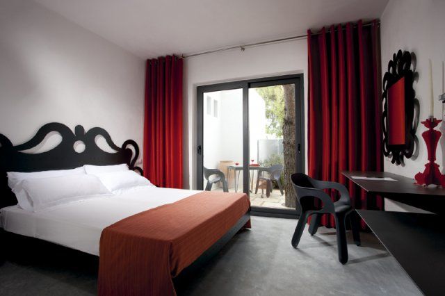 Camera con letto matrimoniale, copriletto rosso, tendaggi rossi, e porta finestra con vista cortile.