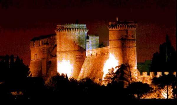 Un castello medievale illuminato di notte, con torri robuste e mura imponenti.