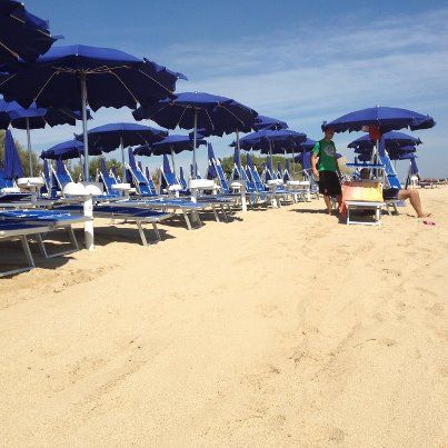 Una spiaggia con file di ombrelloni blu e sdraio, cielo sereno.