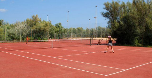 Due persone che giocano a tennis su un campo all'aperto circondato da alberi.