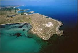 Veduta aerea di una penisola con mare azzurro e costa rocciosa.